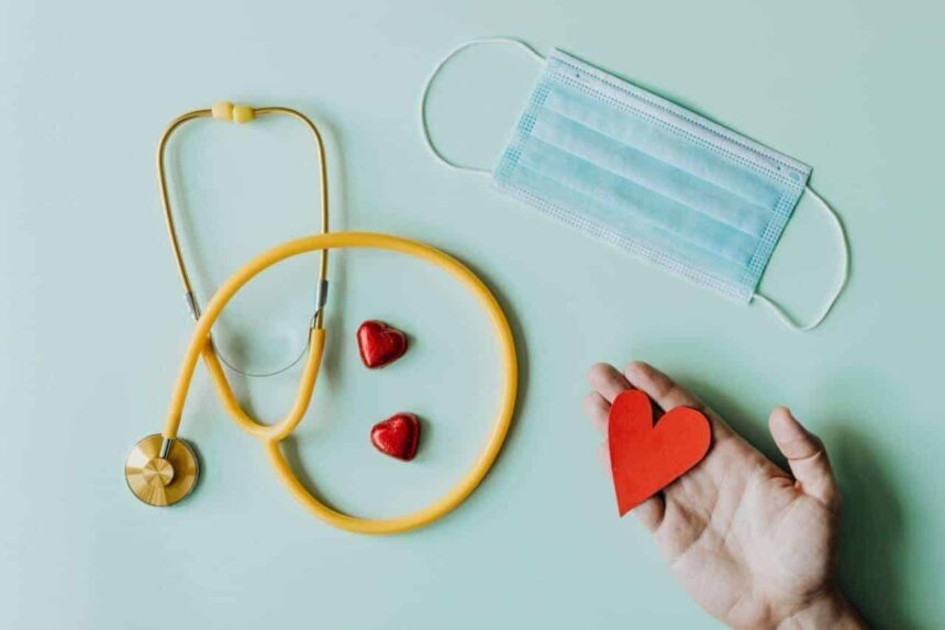 A stethoscope, medical mask, candy hearts, and an open hand with a red paper heart in it.