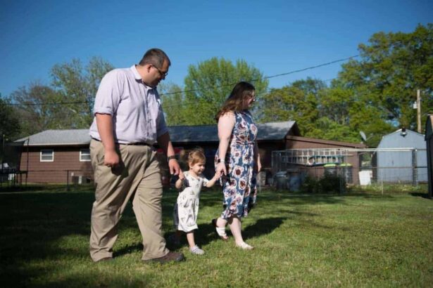 Parents holding hands with their young child between them walks through the front yard of their home