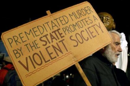 A pro-life protestor with a sign that says “PREMEDITATED MURDER BY THE STATE PROMOTES A VIOLENT SOCIETY”
