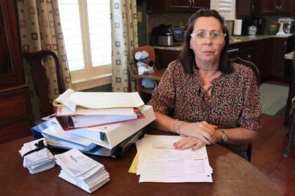 A woman sits at a table with stacks of medical bills in front of her.