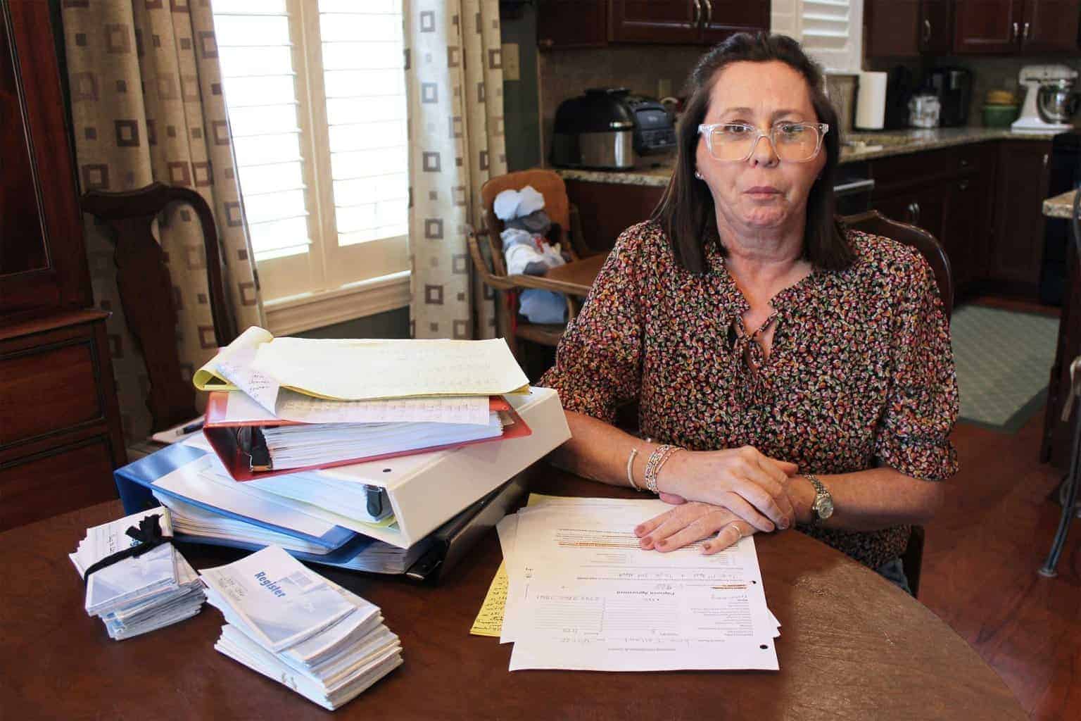 A woman sits at a table with stacks of medical bills in front of her.