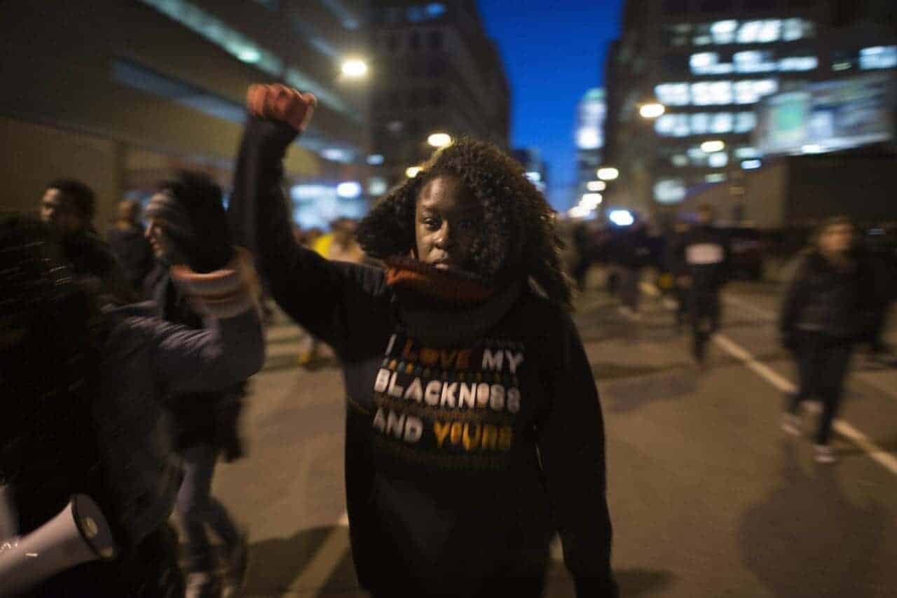 A black lives matter protester in the street wearing a sweatshirt that says “i am proud of my blackness and my values. ”