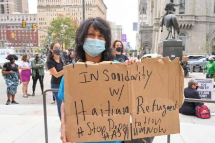 A woman holding a cardboard sign during a protest in Philadelphia against deportation of Haitian migrants.