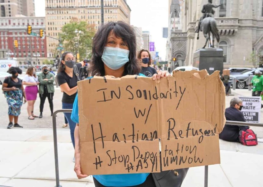 A woman holding a cardboard sign during a protest in philadelphia against deportation of haitian migrants.