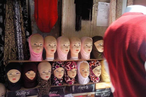 A woman wearing a hijab looks at a store shelf of mannequin heads displaying hijabs.