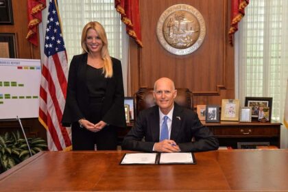 Pam Bondi stands beside Governor Rick Scott during a bill signing.