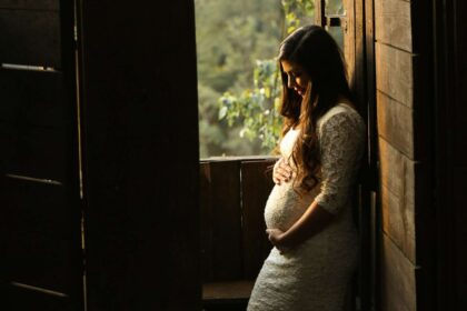 Pregnant woman standing in the sun by a window in a barn