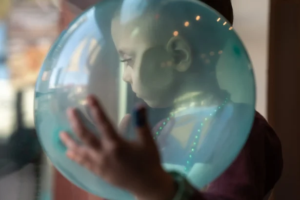 August looks through the glass door of the birthday venue while cradling a balloon on dec. 9, 2023. He had inoperable brain cancer and depended on medicaid to pay for full-time home nursing care from a private agency to help his mother take care of him throughout years of health crises