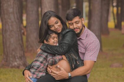 Latino family with husband and small child hugging pregnant woman