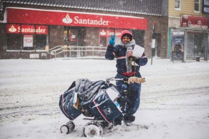 USPS worker standing in the snow-covered street, waves and smiles