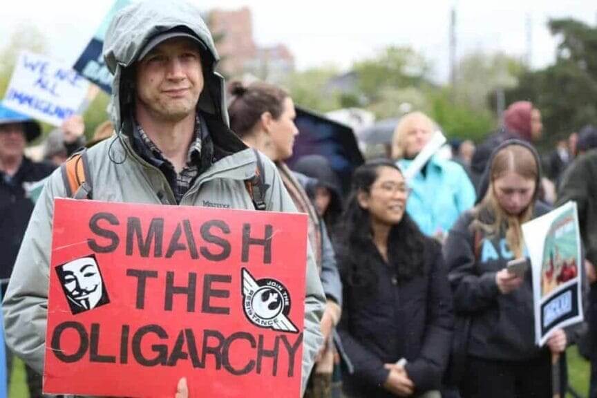 Protest with young man holding a sign that says smash the oligarchy