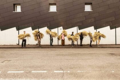 People walking down the street carrying sheaves of wheat