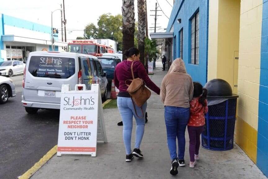 Community health clinic workers prepare to protect families family walking on the sidewalk in front of a city health clinic