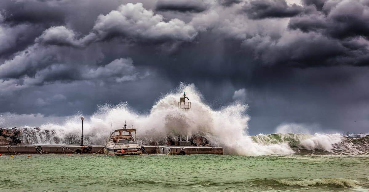 Powerful waves crash against a pier and lighthouse under dark stormy skies.