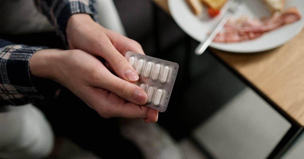 Close-up of a person holding a blister pack of pills with breakfast in the background, indicating medication and daily routine.