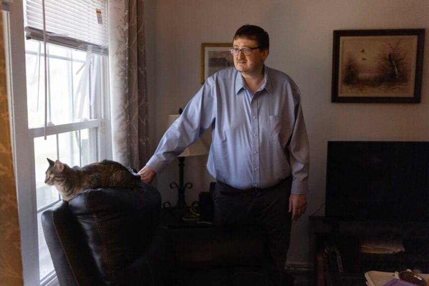 eric wunderlin with his cat Medicaid work requirements have caused issues for this man, standing next to his cat laying on the back of an a recliner.
