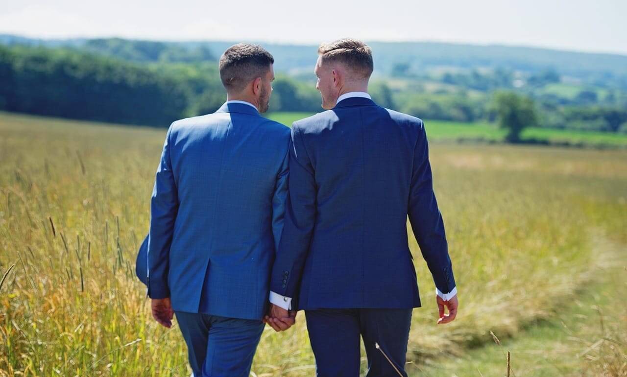 Same-sex marriage a male couple walks through a field holding hands