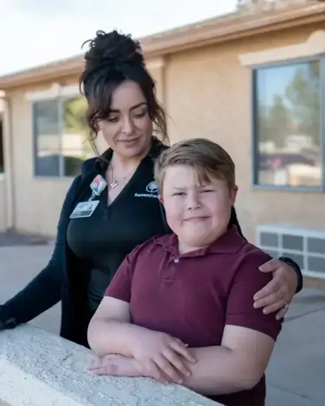 mother and son Border security doesn't replace access to medical treatment, mother and son stand side by side with her arm around his shoulder. He smiles at the camera as she looks down at him.