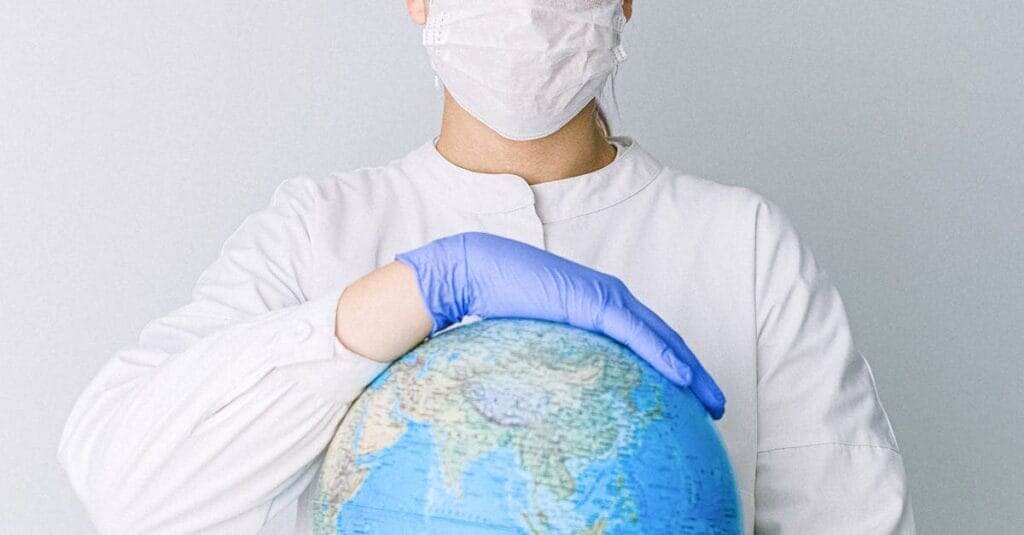 A medical professional wearing a mask and gloves holds a globe, symbolizing global health care during a pandemic.