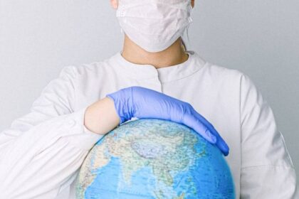 A medical professional wearing a mask and gloves holds a globe, symbolizing global health care during a pandemic.