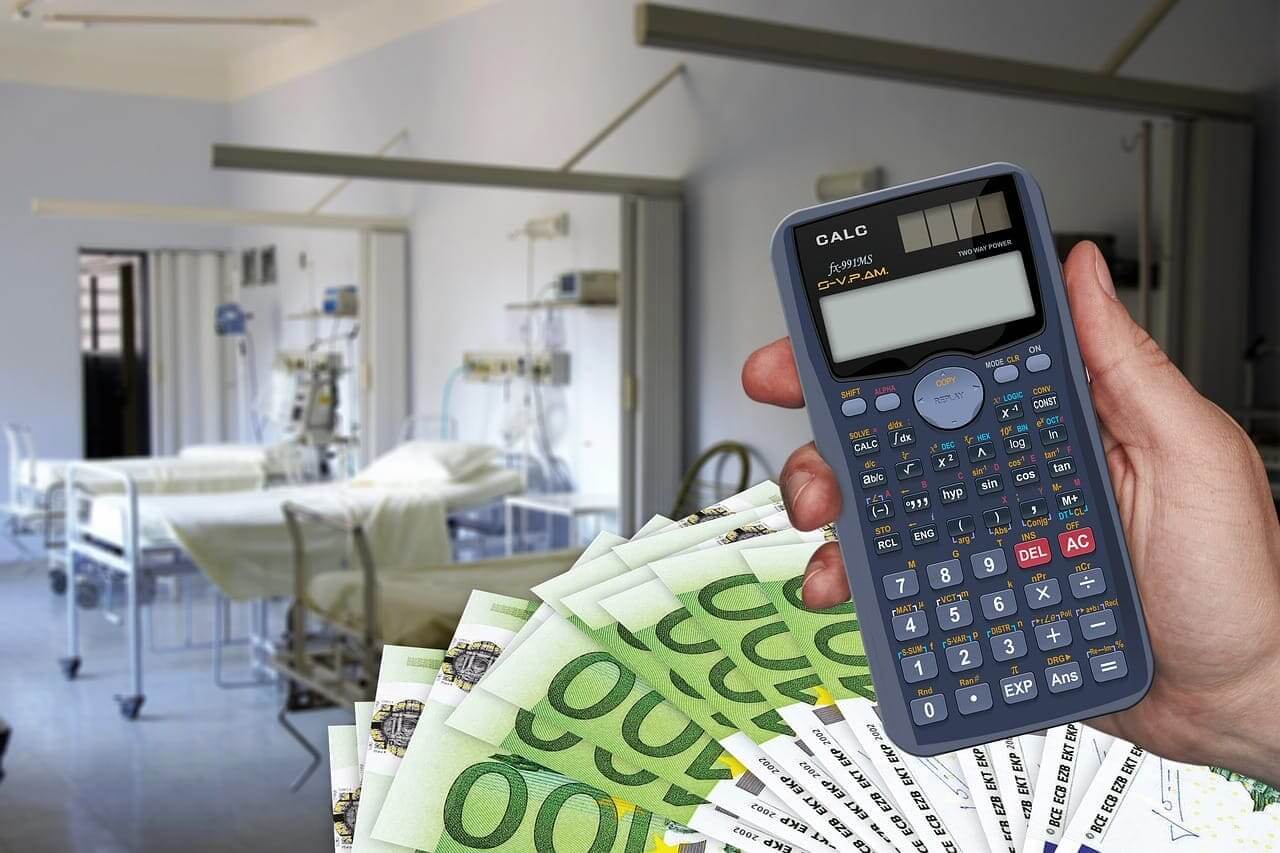 A hospital room in the background with a calculator and cash in the foreground