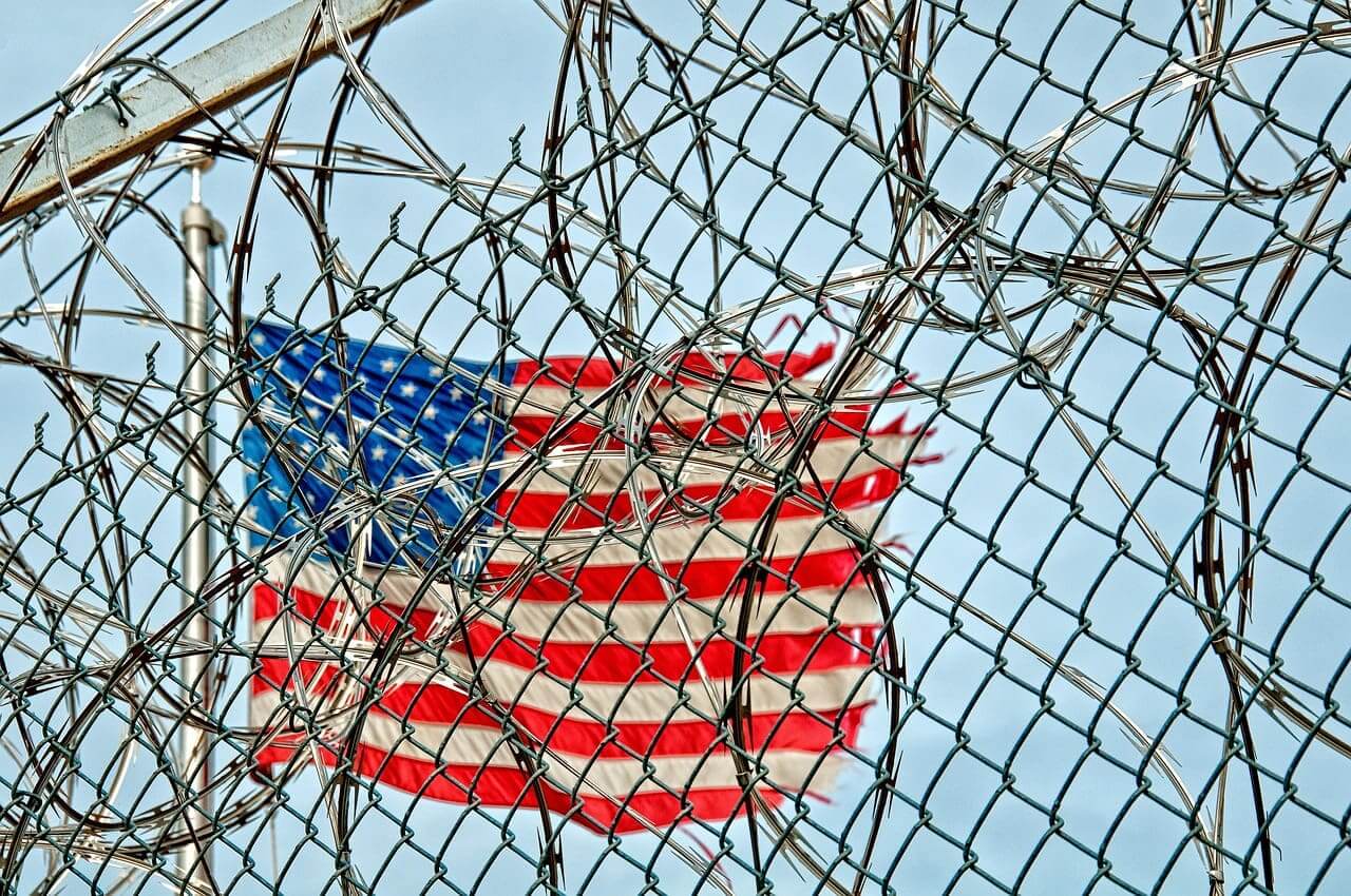 Razorwire and fencing in front of a torn american flag