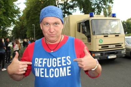Man wearing a blue tank top with white text “REFUGEES WELCOME”