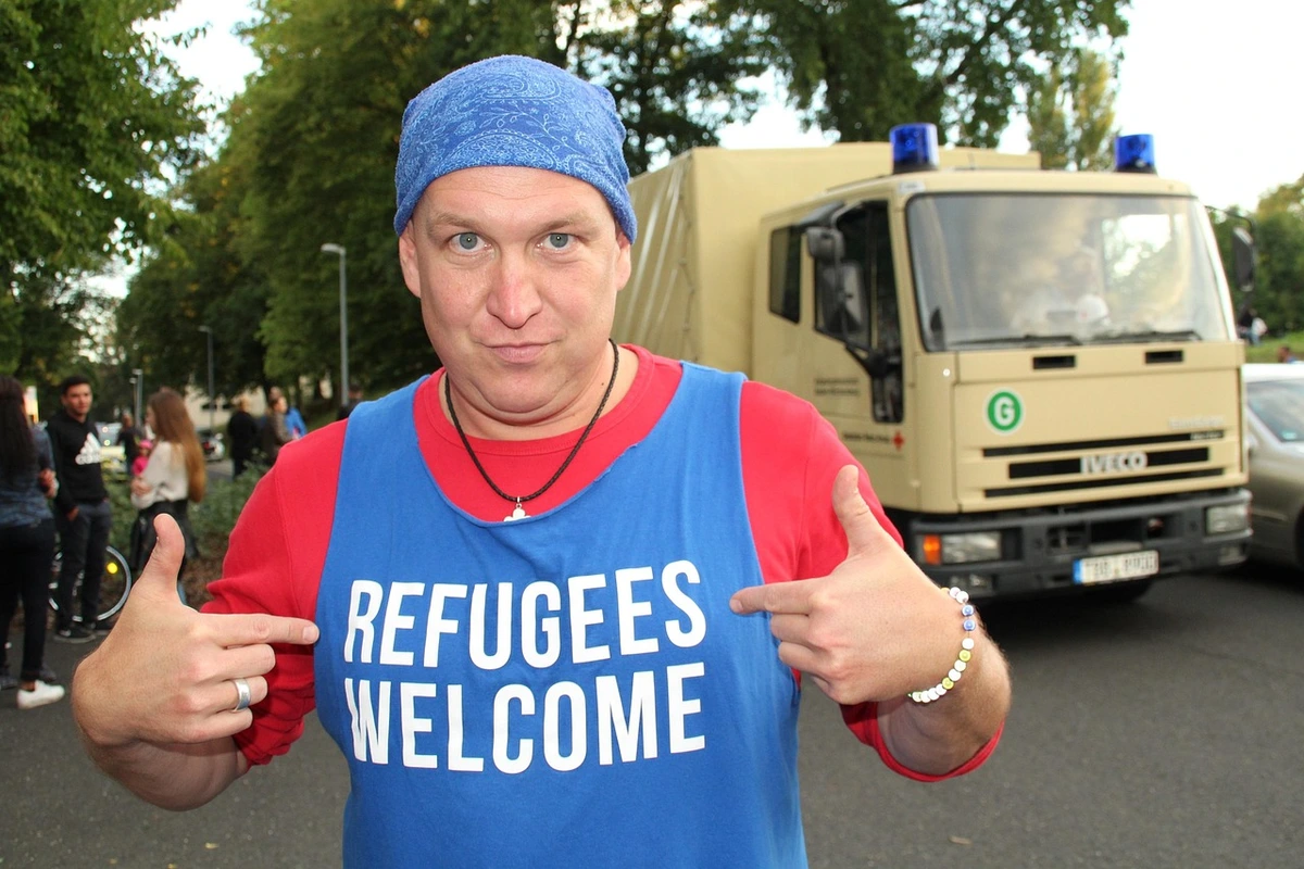 Man wearing a blue tank top with white text “REFUGEES WELCOME”